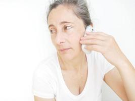 mujer de cuarenta y nueve años con una camiseta blanca sobre un fondo blanco hablando por su celular foto