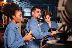 Multiracial professional industry engineer teams in safety uniforms work by inspecting machines' voltage current, checking, and maintaining at manufacture factory, electric system service occupations. photo