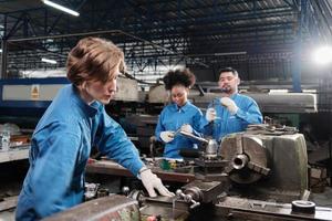 joven trabajadora de la industria caucásica trabaja con herramientas de precisión de metalistería, máquinas de torno y taller de piezas de repuesto con un equipo multirracial en la fábrica de fabricación, ingenieros mecánicos profesionales. foto