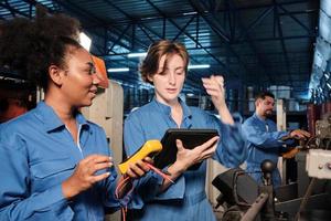 Two professional female engineer workers in safety uniforms work by inspecting machines' voltage current, checking, and maintaining at manufacturing factory, electric system service occupations. photo