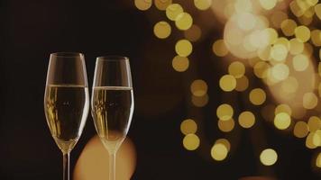 Two glass of champagne on gold bokeh background of golden shiny glares. video