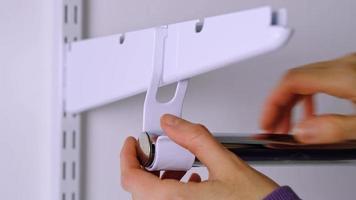 Installation brackets of a metal mesh shelf in the dressing room system on a bracket. Hands is assembling a white holder storage system close-up video