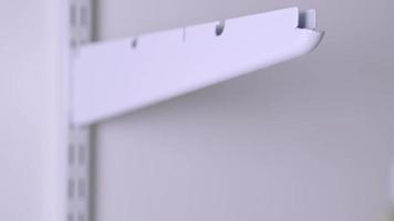 Installation brackets of a metal mesh shelf in the dressing room system on a bracket. Hands is assembling a white holder storage system close-up video