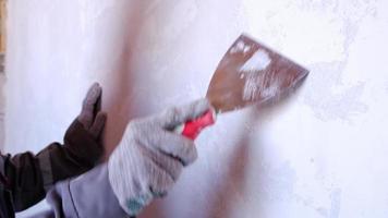 preparación y limpieza de paredes para reparación y acabado con espátula con yeso y masilla antes de pintar. una mujer con gorra roja y uniforme de construcción está preparando el acabado de las paredes video