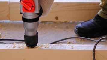 Drilling holes in wooden floor logs of the house with a puncher drill for the installation floor brackets, sawdust is flying. Forstner wood drill, feather. Construction and repair with your own hands video