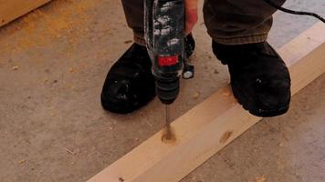 Drilling holes in wooden floor logs of the house with a puncher drill for the installation floor brackets, sawdust is flying. Forstner wood drill, feather. Construction and repair with your own hands