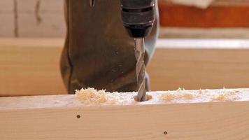 Drilling holes in wooden floor logs of the house with a puncher drill for the installation floor brackets, sawdust is flying. Forstner wood drill, feather. Construction and repair with your own hands