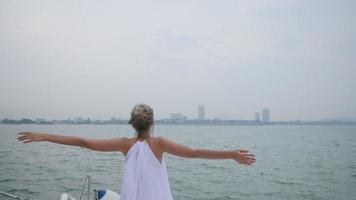 beautiful woman in white dress on a sailboat with free carefree happy girl looking at ocean with open arms, slow-motion shot video