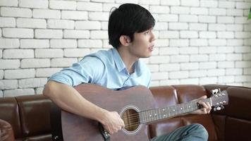 young Asian man playing guitar music and sing a song relax to record video live streaming, musician artist work from home, new normal lifestyle on cyberspace online communication