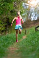 Blonde girl athlete running in a trail into the woods photo