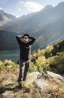 joven turista con una gorra con las manos arriba en la cima de las montañas foto