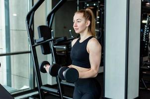 A young girl in black sportswear is engaged in the gym with dumbbells. Fitness club concept. photo
