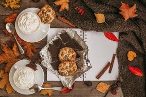 Autumn, fall leaves, hot steaming cup of coffee and a warm scarf on wooden table background. photo