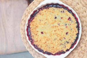 Berry crumble pie in baking dish on natural placemat on a table. summer dessert. cobbler pie with fresh garden grown berries. photo