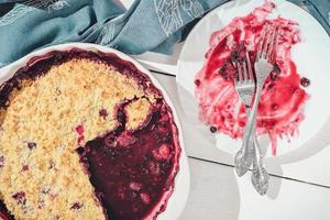 Top view of an empty plate with forks on it after pie. part of a crumble berry pie has been eaten. wooden table, close up photo