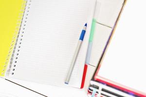 open blank notepad with pen and stack of books. white table, working space, learning and education mock up. copy space. top view photo