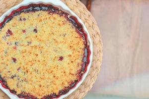 round berry pie in baking dish on placemat. crumble blueberry cobbler. home baking, healthy meal, sugar free food. photo