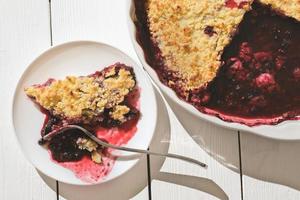 piece of traditional british berry crumble pie, cranberry and raspberry cake on a plate and in baking dish. lifestyle shot. photo