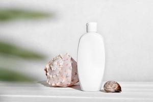 white bottle of cosmetic sunscreen lotion or body moisturizing cream next to seashells. mockup template for summer skin protection with UV screen photo