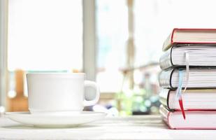 taza de café clásica blanca sobre una mesa blanca en la terraza y una pila de libros con marcadores. aprendizaje de lectura y estudio, horas de la mañana para la autoeducación foto