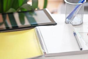 tablet computer and opened paper notepad on a table with stationary. learning and education concept copy space for message. photo