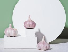 The whole unpeeled garlic on white geometric podium or pedestal. raw garlic, cooking and spice concept. trendy food shot. photo