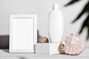 white bottle of cosmetic sunscreen lotion or body moisturizing cream next to seashells. mockup template for summer skin protection with UV screen, White frame for text photo