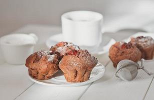 muffins de chocolate caseros con relleno de bayas y una taza de café sobre una mesa de madera. repostería casera, sabroso desayuno para el fin de semana. foto