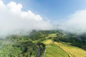 Aerial view drone shot of flowing fog waves on mountain tropical rainforest,Bird eye view image over the clouds Amazing nature background with clouds and mountain peaks in Nan Thailand. photo