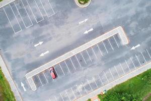 Aerial view top down of red SUV car parked at concrete car parking lot with white line of traffic sign on the street. Above view of car in a row at parking space Outside car parking area photo