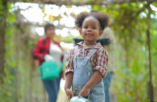 Litte Afro Kid Farmer Girl In garden watering plants and Harvest vegetables. photo