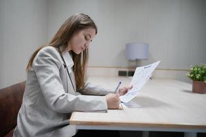 Young businesswoman at workplace and reading paper in office photo