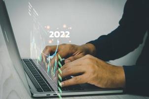 análisis de las tendencias de crecimiento empresarial y las finanzas de la empresa hombre de negocios que trabaja en una computadora portátil con gráfico y gráfico de pantalla virtual. flecha apuntando a 2022 foto