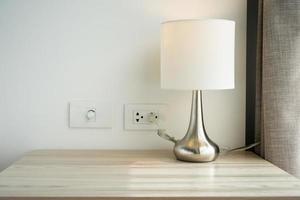 A white table lamp adorns the bedroom next to a glass door with a curtain during daylight hours. photo