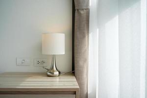 A white table lamp adorns the bedroom next to a glass door with a curtain during daylight hours. photo