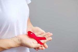 mano sosteniendo la cinta roja para el día mundial del sida de diciembre, el mes de concientización sobre el cáncer de mieloma múltiple y la semana nacional de la cinta roja. concepto de salud y día mundial del cáncer foto