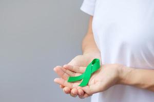 Hand holding green Ribbon for Liver, Gallbladders, bile duct, cervical, kidney Cancer and Lymphoma Awareness month. Healthcare and world cancer day concept photo