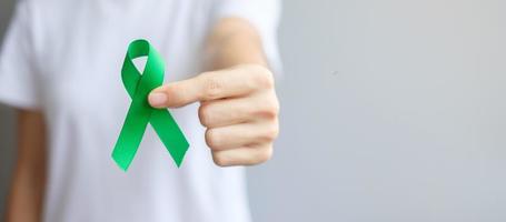 Hand holding green Ribbon for Liver, Gallbladders, bile duct, cervical, kidney Cancer and Lymphoma Awareness month. Healthcare and world cancer day concept photo