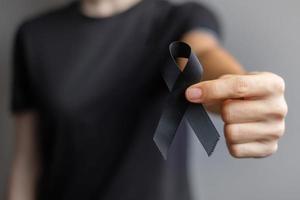 mujer con cinta negra para melanoma y cáncer de piel, mes de concientización sobre lesiones por vacunas, dolor y descanso en paz. salud y concepto racista foto