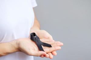 Woman holding black Ribbon for Melanoma and skin cancer, Vaccine injury awareness month, grief and rest in peace. Healthcare and Racist concept photo