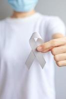 mes de concientización sobre el cáncer cerebral, mano de mujer sosteniendo una cinta de color gris para apoyar a las personas que viven. concepto de salud y día mundial del cáncer foto