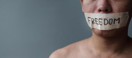Man with mouth sealed in adhesive tape with Freedom message. Free of speech, freedom of press, Human rights, Protest dictatorship, democracy, liberty, equality and fraternity concepts photo