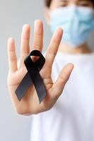 mujer con cinta negra para melanoma y cáncer de piel, mes de concientización sobre lesiones por vacunas, dolor y descanso en paz. salud y concepto racista foto