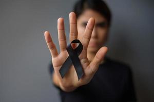 Woman holding black Ribbon for Melanoma and skin cancer, Vaccine injury awareness month, grief and rest in peace. Healthcare and Racist concept photo