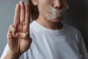 Woman show three finger with mouth sealed in adhesive tape. Freedom of speech, Human rights, Protest dictatorship, democracy, liberty, equality and fraternity concepts photo