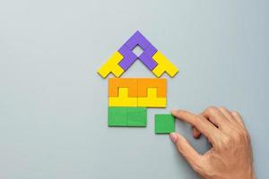 hand connecting Home shape block with colorful wood puzzle pieces on gray background. logical thinking, business logic, solutions, rational, house, real estate and strategy concepts photo