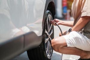 hombre conductor inflando a mano los neumáticos del vehículo, quitando la tapa de nitrógeno de la válvula del neumático para comprobar la presión del aire y llenando el aire en la rueda del coche en la gasolinera. autoservicio, mantenimiento y seguridad foto