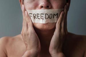 Man with mouth sealed in adhesive tape with Freedom message. Free of speech, freedom of press, Human rights, Protest dictatorship, democracy, liberty, equality and fraternity concepts photo