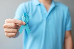 noviembre mes de concientización sobre el cáncer de próstata, hombre con camisa azul con la mano sosteniendo una cinta azul para apoyar a las personas que viven y están enfermas. cuidado de la salud, hombres internacionales, padre y concepto del día mundial del cáncer foto