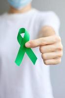 Hand holding green Ribbon for Liver, Gallbladders, bile duct, cervical, kidney Cancer and Lymphoma Awareness month. Healthcare and world cancer day concept photo